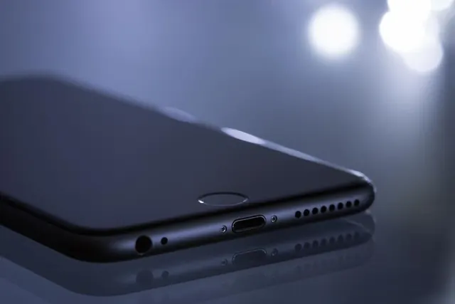 Celular negro sobre una superficie reflectante, primer plano